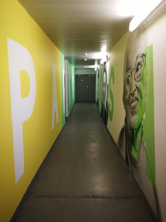 Couloir avec des murs peints en jaune et des inscriptions "PARIS" et un portrait en vert.